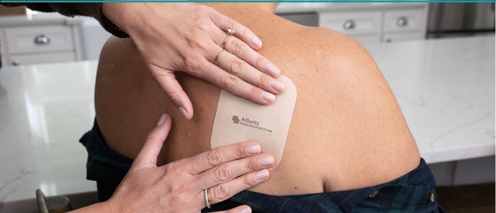 Image of caregiver applying ADLARITY to patient's upper back, right side